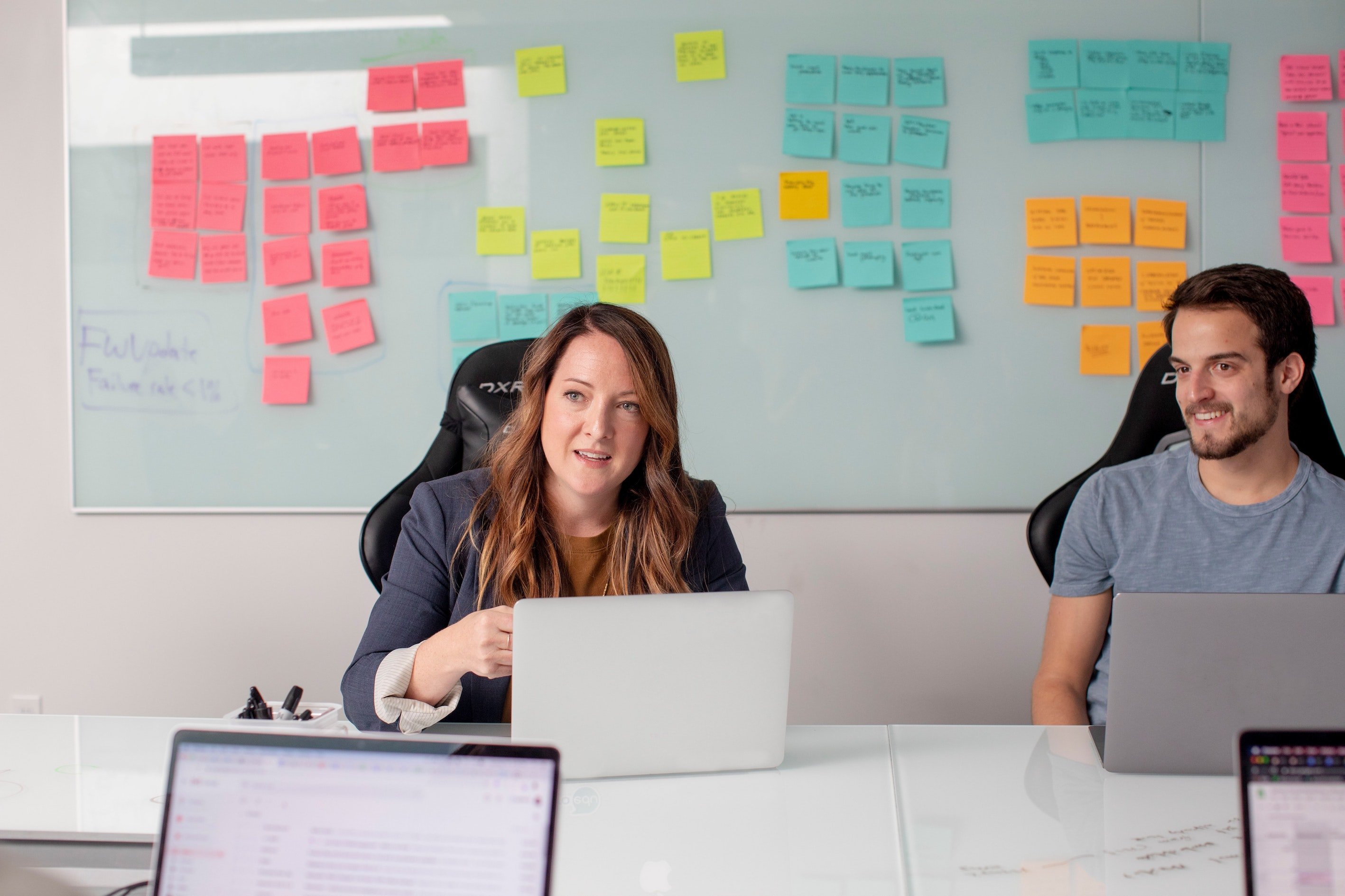 Man and woman sitting at laptops with post it notes on whiteboard behind them