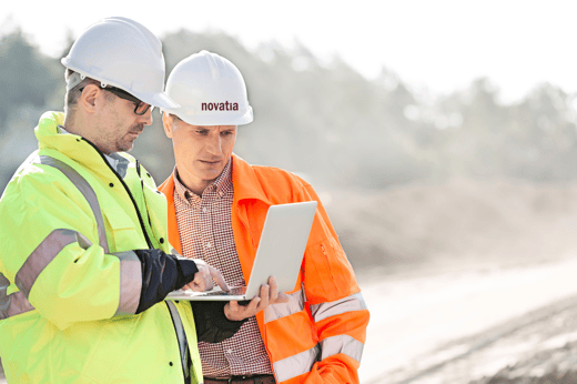 two men outside in hi viz with hats and laptop